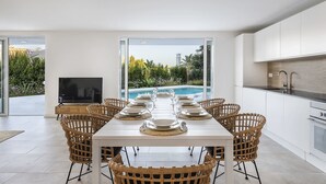 Un moderno comedor con vistas a la piscina, muebles de cocina blancos y sillas de mimbre.
