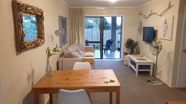 A cozy living room with a wooden table, a sofa, and a sliding glass door leading to a patio. - Private guest suite on the North Shore (Auckland)