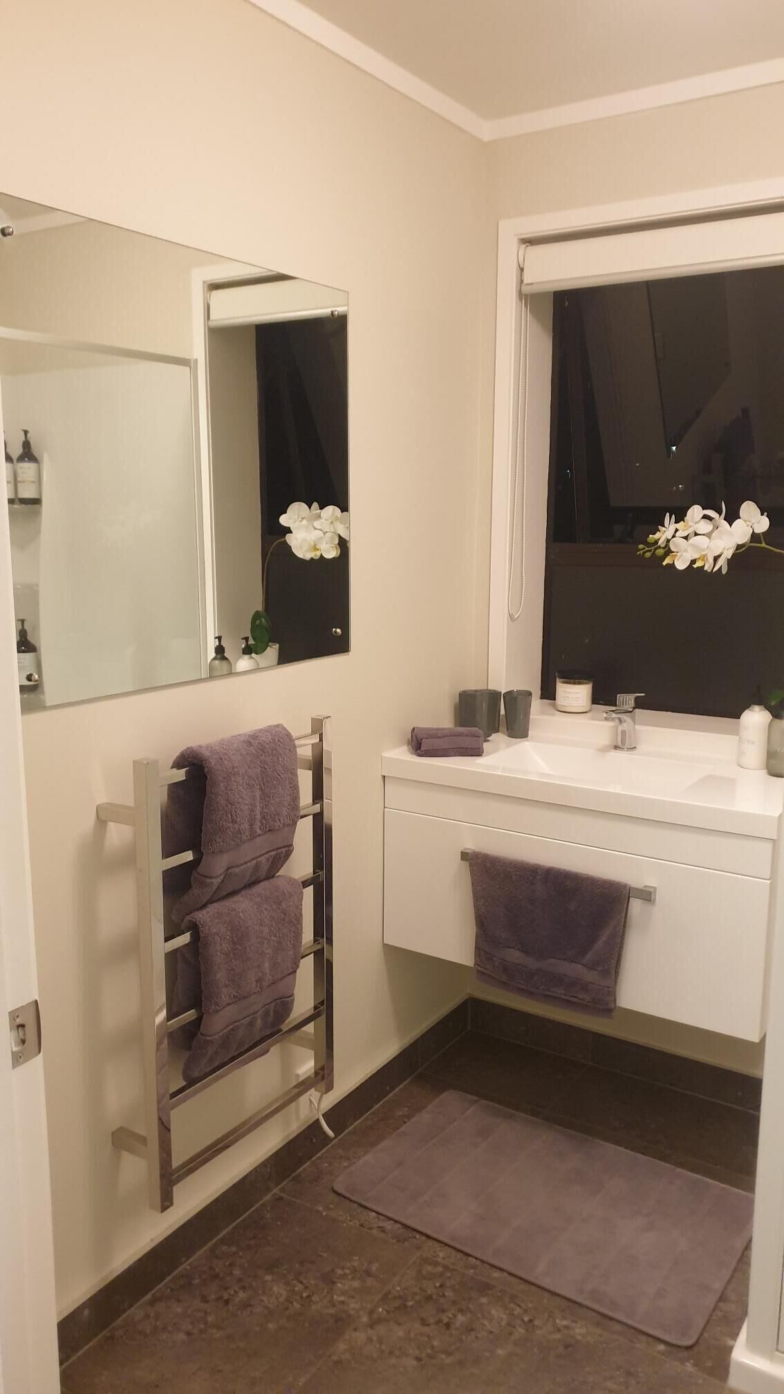 A bathroom with a white vanity, a towel rack with multiple towels, a mirror, and a window with a view of the night sky.
