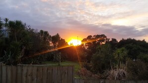 A sunset over a residential area with a wooden fence and dense foliage. - Private guest suite on the North Shore (Auckland)