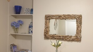 A room with a mirror framed by natural materials, a vase with flowers, and shelves with decorative items and books. - Private guest suite on the North Shore (Auckland)