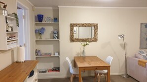 A cozy room with a wooden dining table, white chairs, a mirror with a natural frame, and shelves with various items. - Private guest suite on the North Shore (Auckland)