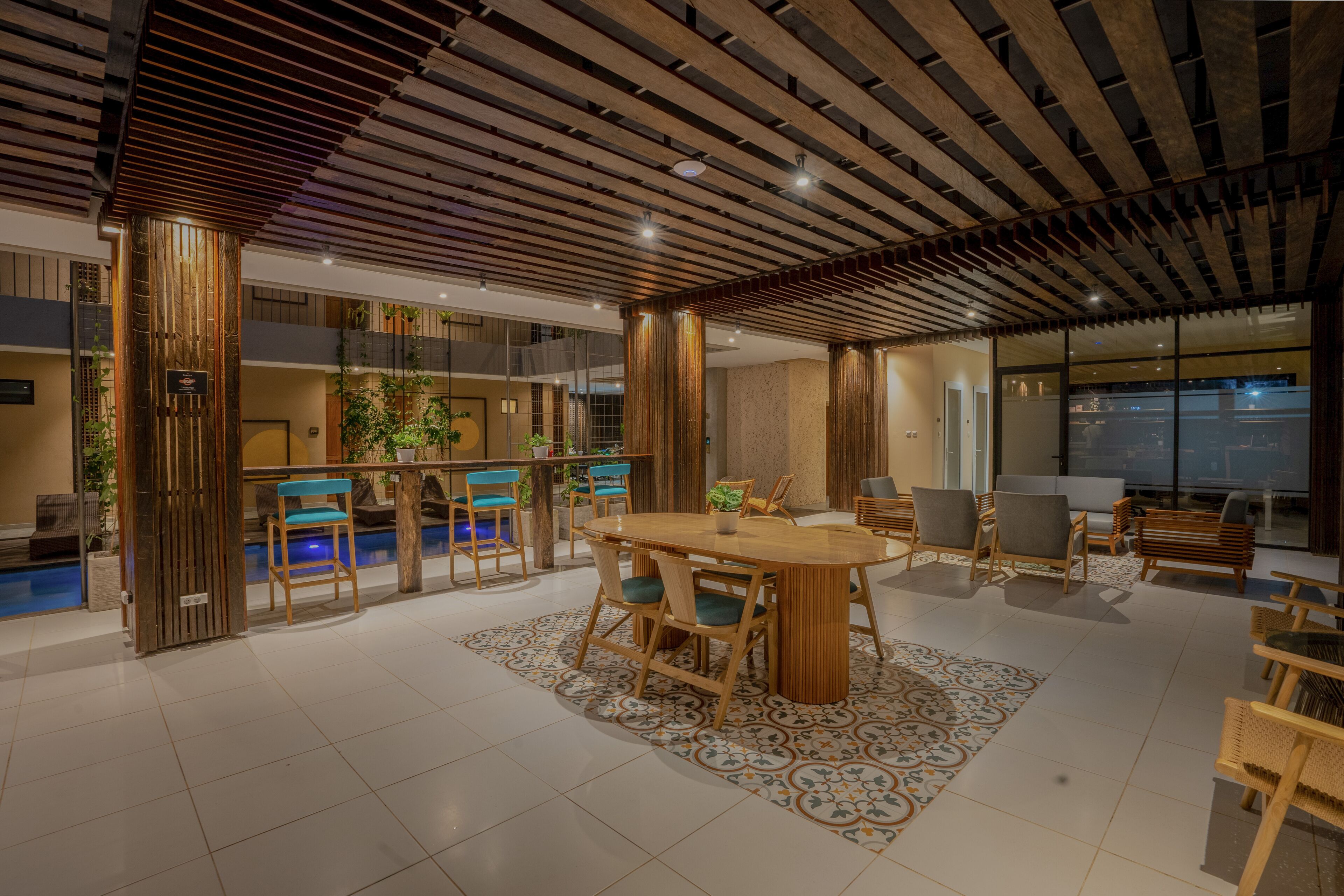 A spacious indoor area with a wooden ceiling, a pool, and a dining area with chairs and a table.
