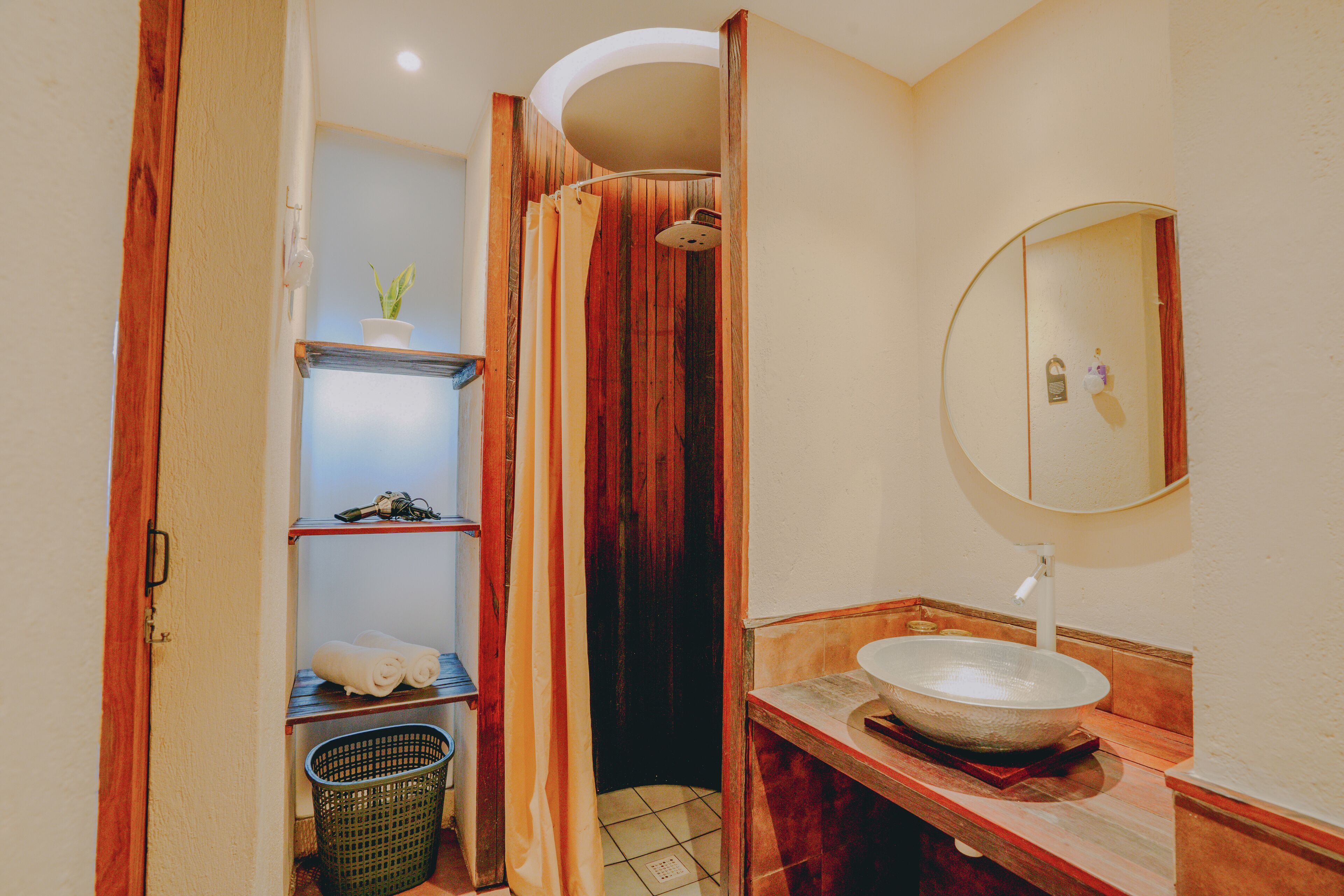 A bathroom with a wooden vanity, a round mirror, a white sink, and a shower curtain.