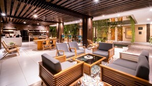 A modern lounge area with wooden furniture, a bar, and a view of greenery. - Tanaga Coliving (Seminyak)