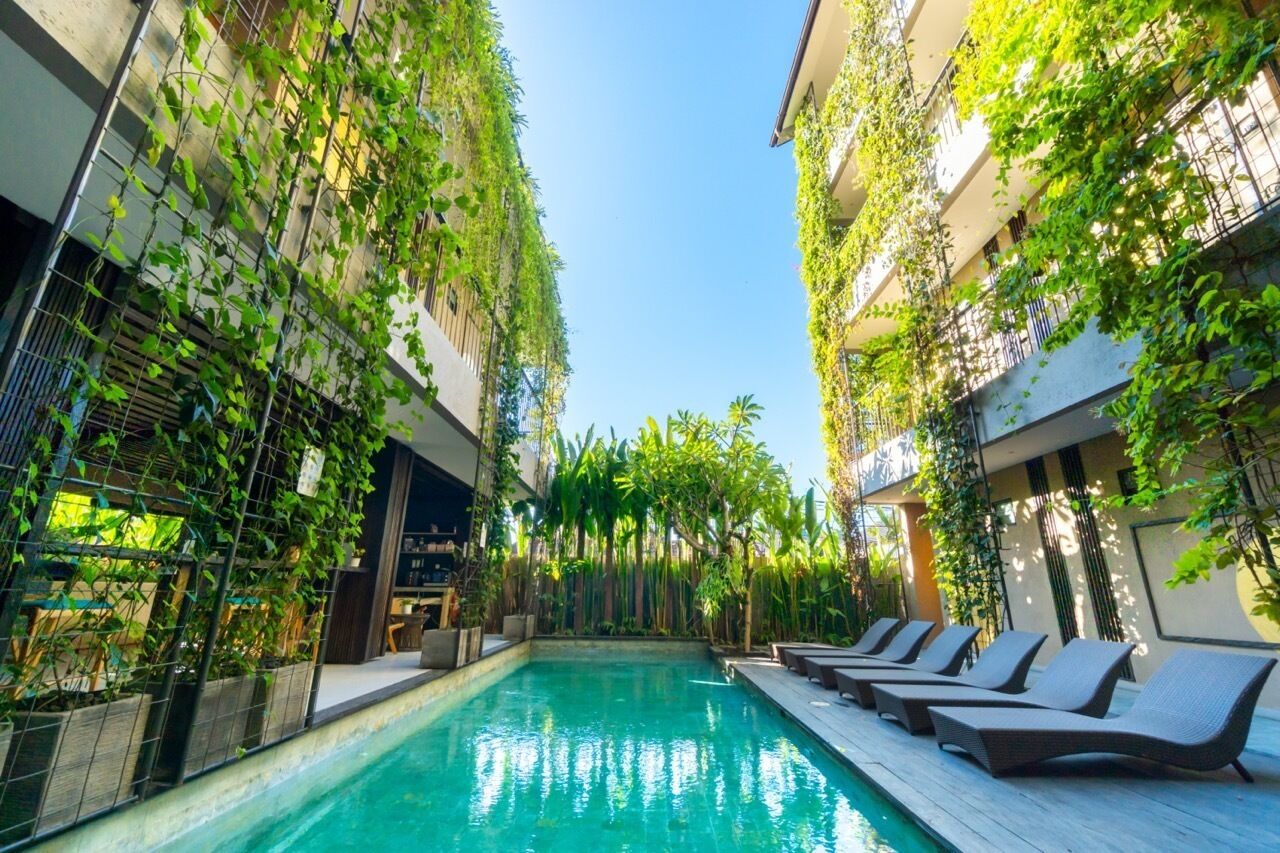 A poolside area with lounge chairs and a pool, surrounded by greenery and buildings.