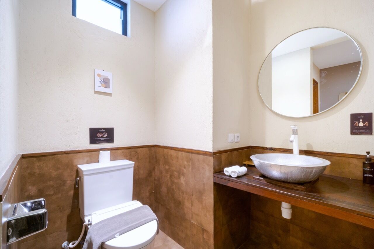 A bathroom with a white toilet, a large oval mirror, and a wooden vanity with a large bowl sink.