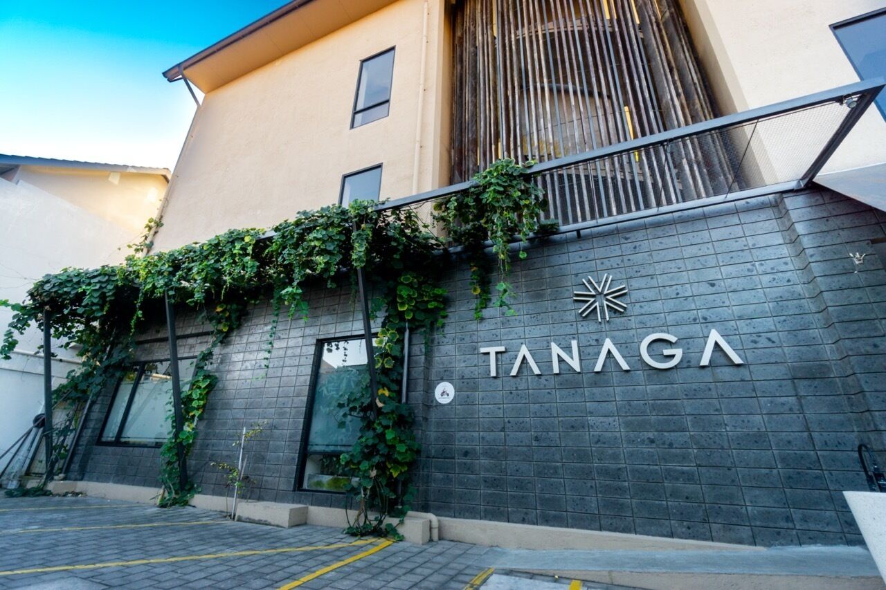 A building with a sign reading "TANAGA" and a modern design with a brick facade and a metal railing.