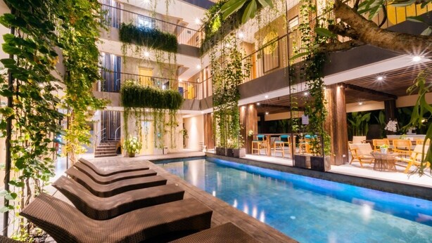 A modern indoor pool area with tiered seating and lush greenery. - Tanaga Coliving (Seminyak)