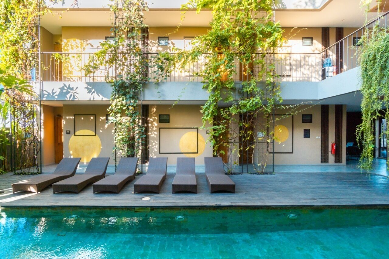 A poolside area with lounge chairs and a view of a building with balconies and greenery.