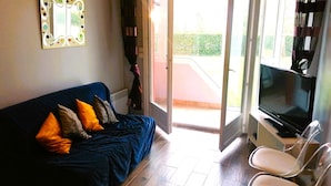 Una sala de estar con un sofá azul oscuro, un televisor de pantalla plana y un ventanal que da a un balcón.