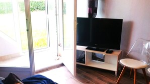 Una habitación con cama, televisor sobre un mueble, una silla y un ventanal corredero que da a un espacio exterior.