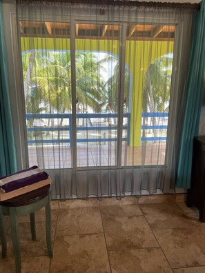 A room with a sliding glass door leading to a balcony with a view of palm trees and a blue railing.