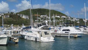 A marina with multiple boats docked, surrounded by a hillside with houses.
