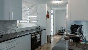 A modern kitchen with white cabinets, a black countertop, stainless steel appliances, and a window with blinds.