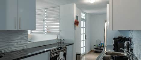 Una cocina moderna con armarios blancos, encimera negra, electrodomésticos de acero inoxidable y una ventana con persianas.