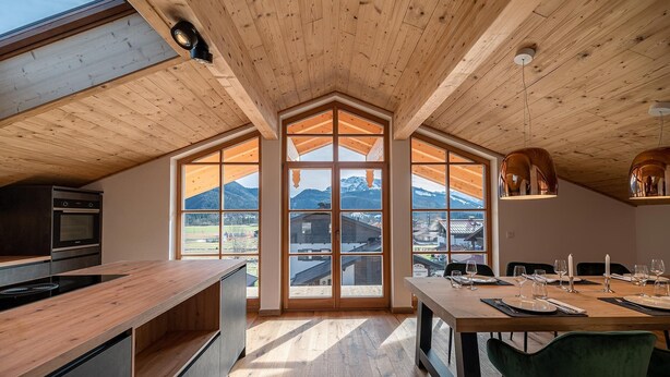 Una cucina moderna con un'ampia finestra, soffitto in legno e un'area pranzo con tavolo imbandito per quattro persone.