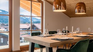 Zona pranzo con tavolo in legno apparecchiato per sei persone, ampie finestre con vista sulle montagne e due lampade a sospensione.