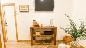 A living room with a flat-screen TV mounted on the wall, a wooden console table with baskets, a patterned rug, and a plant in a glass jar. - Cozy cabin in serene natural setting. Rustic charm with modern amenities! (Franklinton)