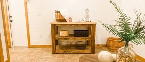 Una sala de estar con una televisión de pantalla plana montada en la pared, una mesa de centro de madera con objetos decorativos, un sofá gris y una alfombra estampada.
