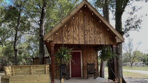A wooden cabin with a porch, a red door, and two chairs. - Cozy cabin in serene natural setting. Rustic charm with modern amenities! (Franklinton)
