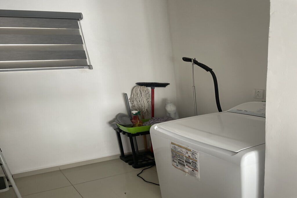 Un espace dédié à la lessive, comprenant un lave-linge, un étendoir et un balai.