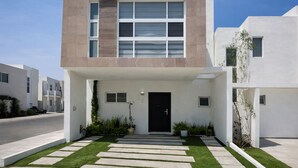 Uma casa moderna de dois andares com porta frontal preta, um pequeno alpendre e gramado bem cuidado.