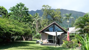 Une maison moderne à la façade en verre, entourée d’une végétation luxuriante et avec des montagnes en toile de fond.