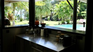 Une cuisine moderne dotée d’une grande fenêtre donnant sur une piscine et une végétation luxuriante.