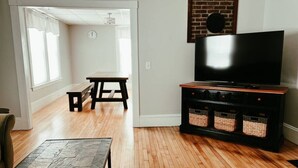 A living room with hardwood flooring, a flat-screen TV on a black stand, a wooden bench, and a stone coffee table.