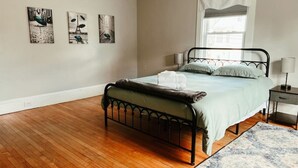 A bedroom with a bed, a nightstand, a window with curtains, and three wall-mounted artworks.