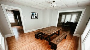 A spacious room with a large wooden dining table and benches, white walls, and a ceiling light fixture.
