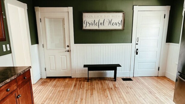 A kitchen with wooden flooring, white cabinetry, and a bench in the center.