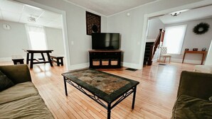 A spacious living room with a wooden floor, a black TV stand, and a green sofa.