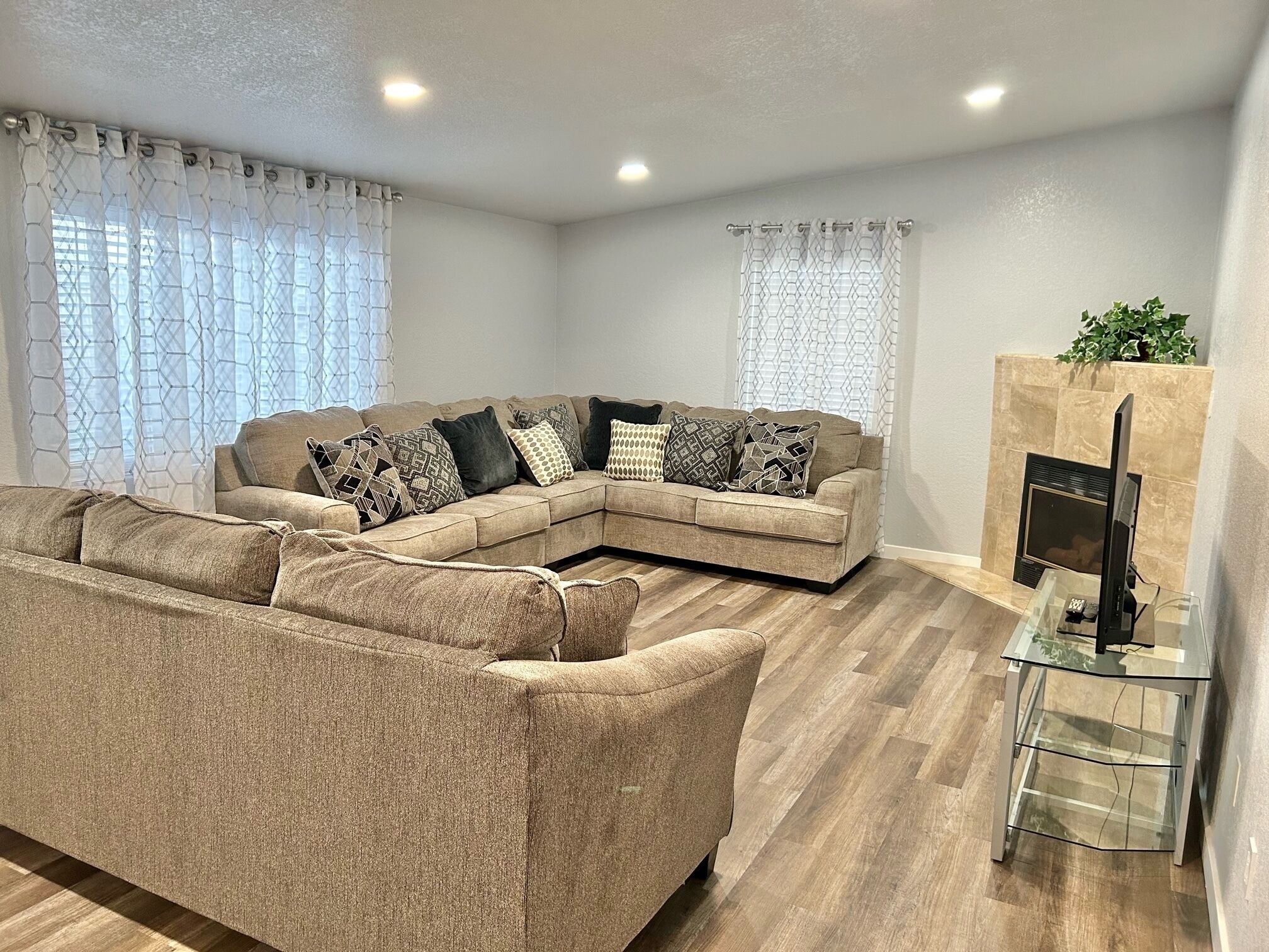 A modern living room with a beige sectional sofa, a glass coffee table, and a fireplace.