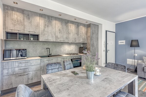 A modern kitchen with grey cabinets, a built-in microwave, and a dining area with a table and chairs. - Porto Letizia Paganini 4, Porlezza, Italy (Porlezza)