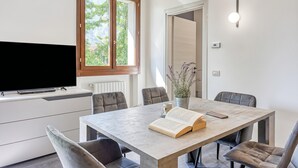 A modern dining area with a table, chairs, a television, and a window with a view of greenery. - Porto Letizia Paganini 4, Porlezza, Italy (Porlezza)