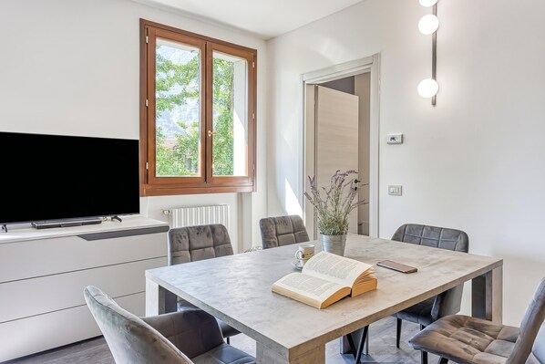 A modern dining area with a table, chairs, a television, and a window with a view of greenery. - Porto Letizia Paganini 4, Porlezza, Italy (Porlezza)