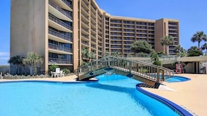 Ein Hotel mit großem Pool, einer Brücke und einer Palme.