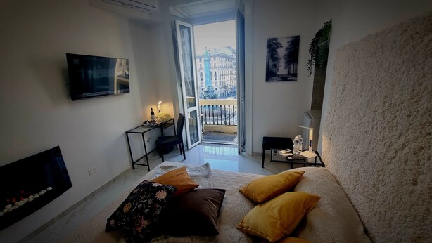Une chambre d’hôtel moderne équipée d’un lit, d’une télévision, d’un bureau avec une lampe et d’un balcon offrant une vue sur la ville.