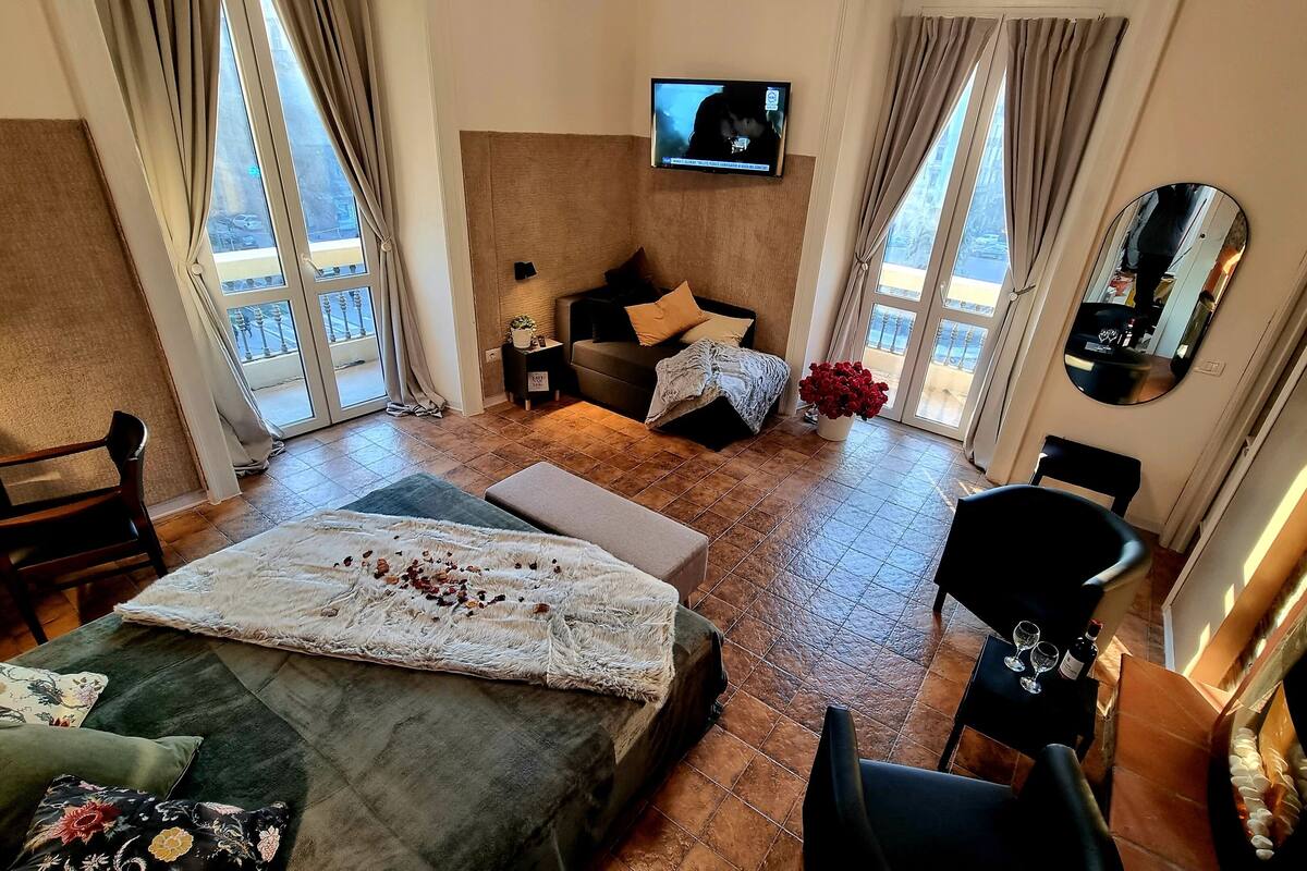 Une chambre d’hôtel avec un lit, un canapé, une télévision, un miroir et un balcon offrant une vue.