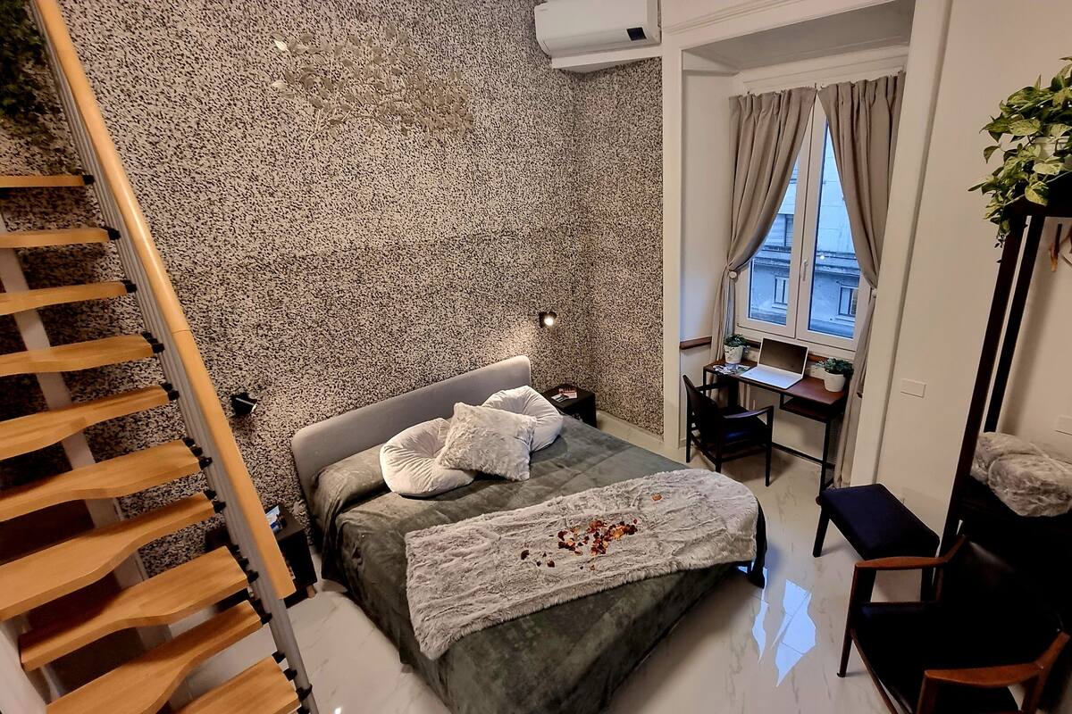 Une chambre à coucher avec un lit, un bureau, une chaise, une plante et une échelle.