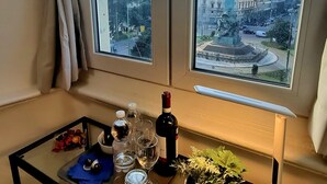 Une pièce avec une grande fenêtre, une table en verre sur laquelle se trouvent une bouteille de vin, des verres et une plante.