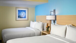 Une chambre d’hôtel avec deux lits, une table de chevet avec une lampe, un tableau encadré au mur et un vase avec des fleurs.