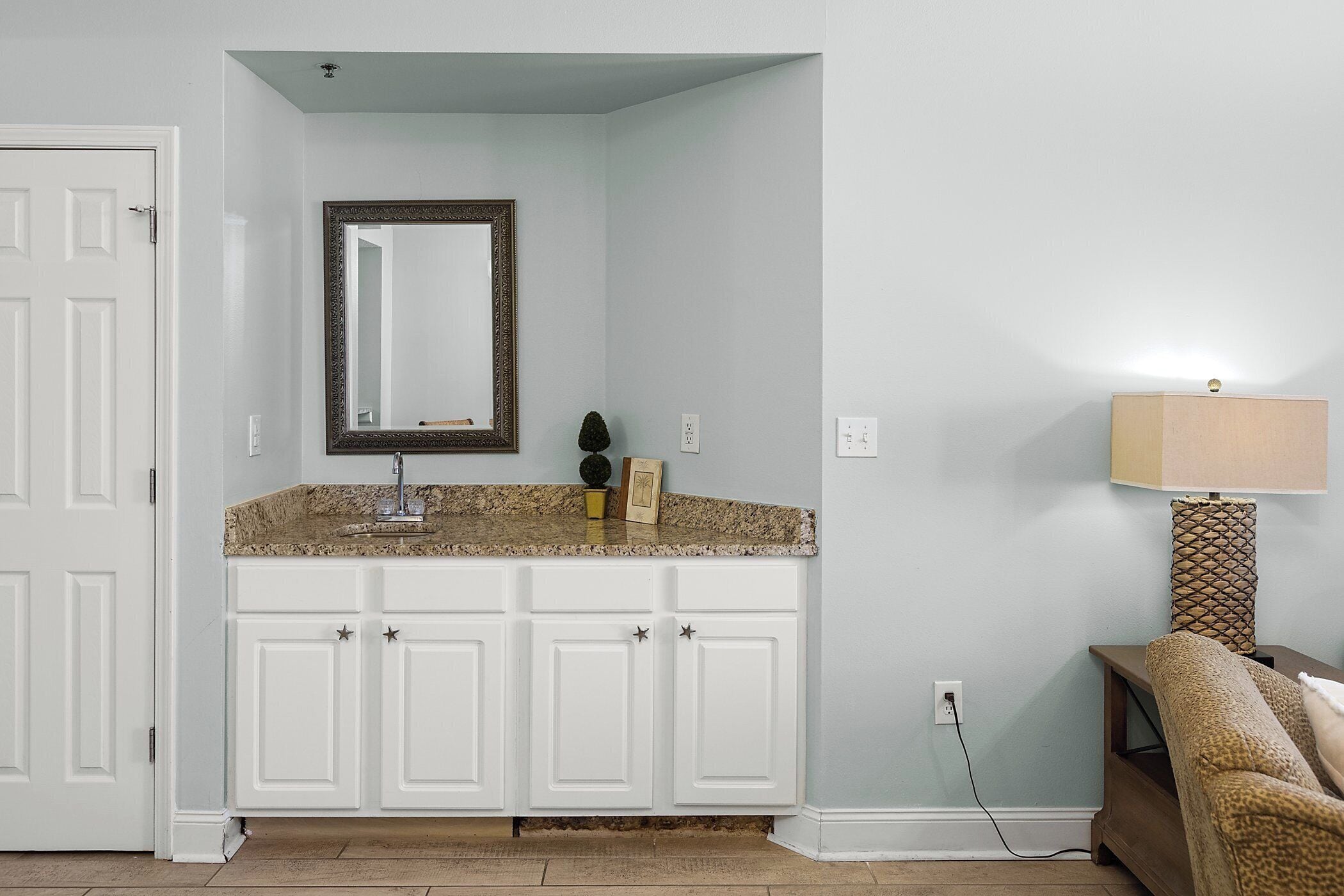 Baño con muebles blancos, encimera de granito, espejo y lámpara.