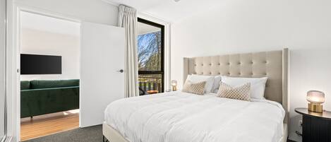 A bedroom with a large bed, a ceiling fan, a bedside table with a lamp, and a view of the outdoors through an open door.