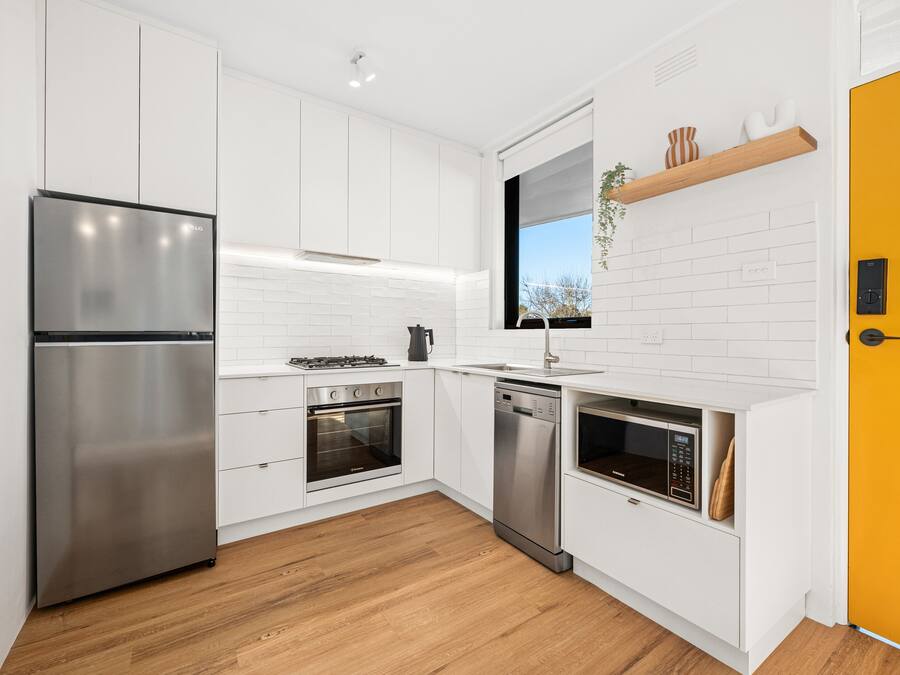 Une cuisine moderne avec des meubles blancs, des appareils en acier inoxydable et un plancher en bois.