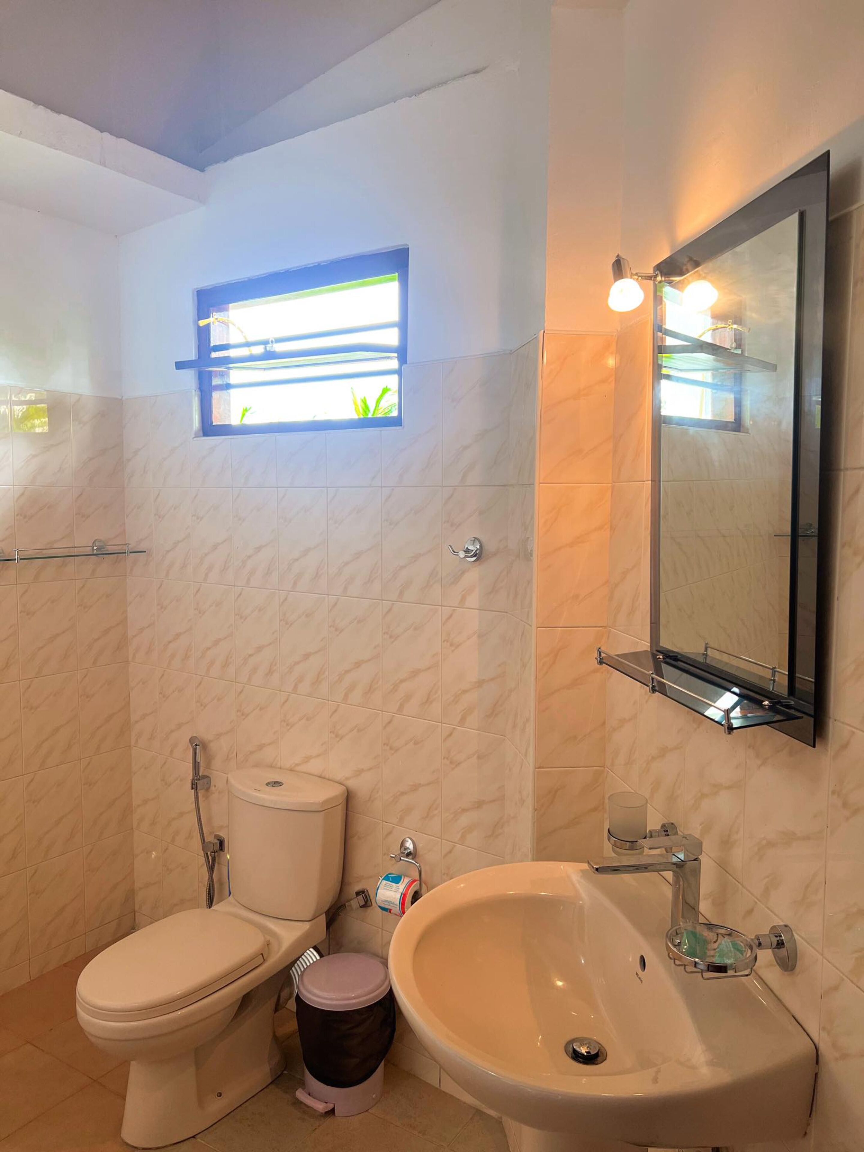 Casa de banho com sanita, bidé, lavatório e uma pequena janela.