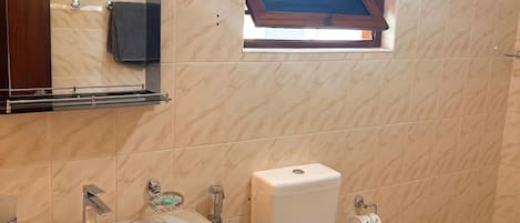A bathroom with a sink, toilet, bidet, and a window with a decorative screen.
