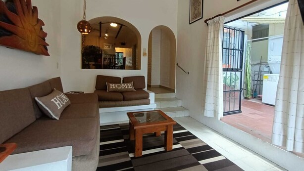 Ein Wohnzimmer mit einer Couch, einem Couchtisch und einem gemusterten Teppich. Eine Treppe führt zu einem Außenbereich.